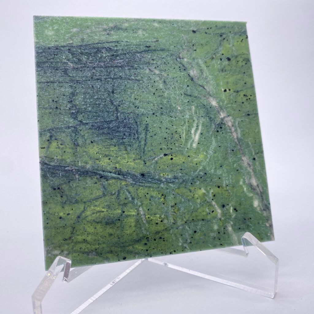 Grüne Steinplatte mit dunklen Adern und schwarzen Flecken, präsentiert auf einem durchsichtigen Acrylständer.