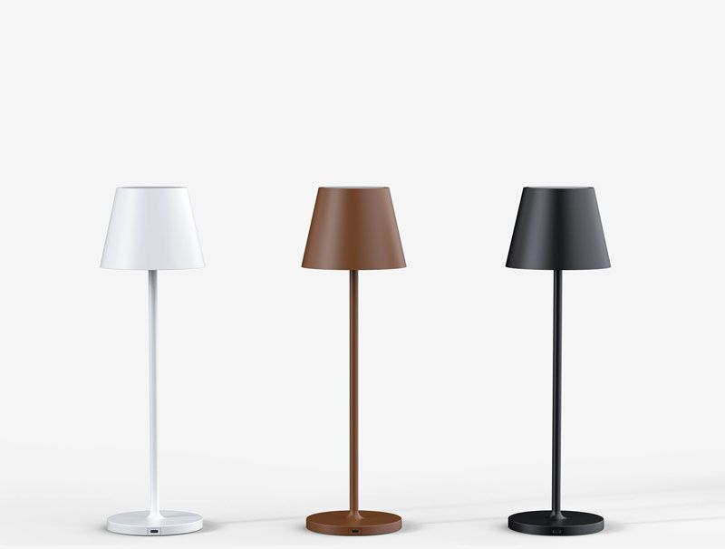Drei moderne Tischlampen: weiß, braun und schwarz, jeweils mit zylindrischem Sockel und Lampenschirm, vor weißem Hintergrund.
