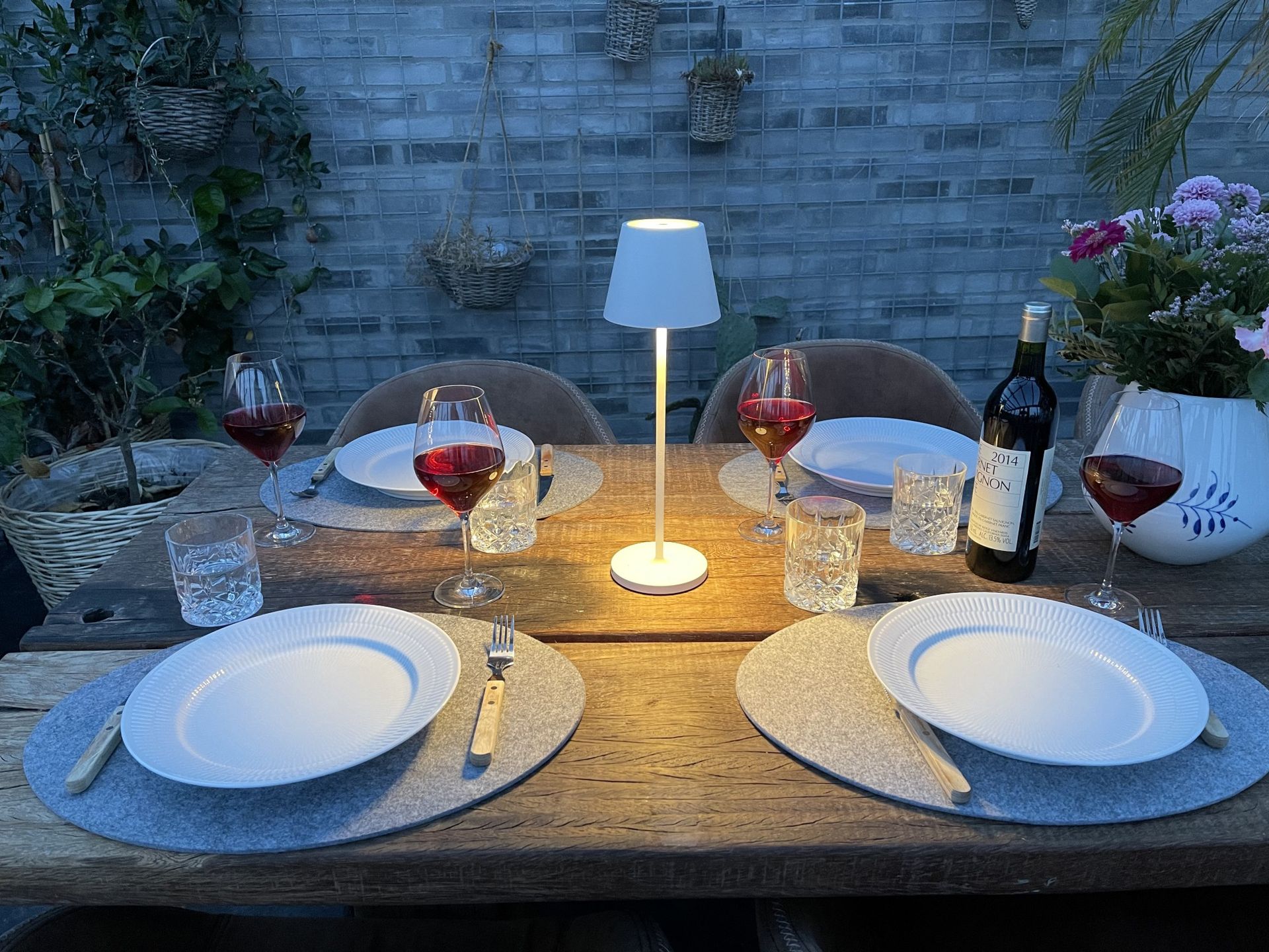 Esstisch für den Außenbereich mit Wein, Tellern und einer Lampe.