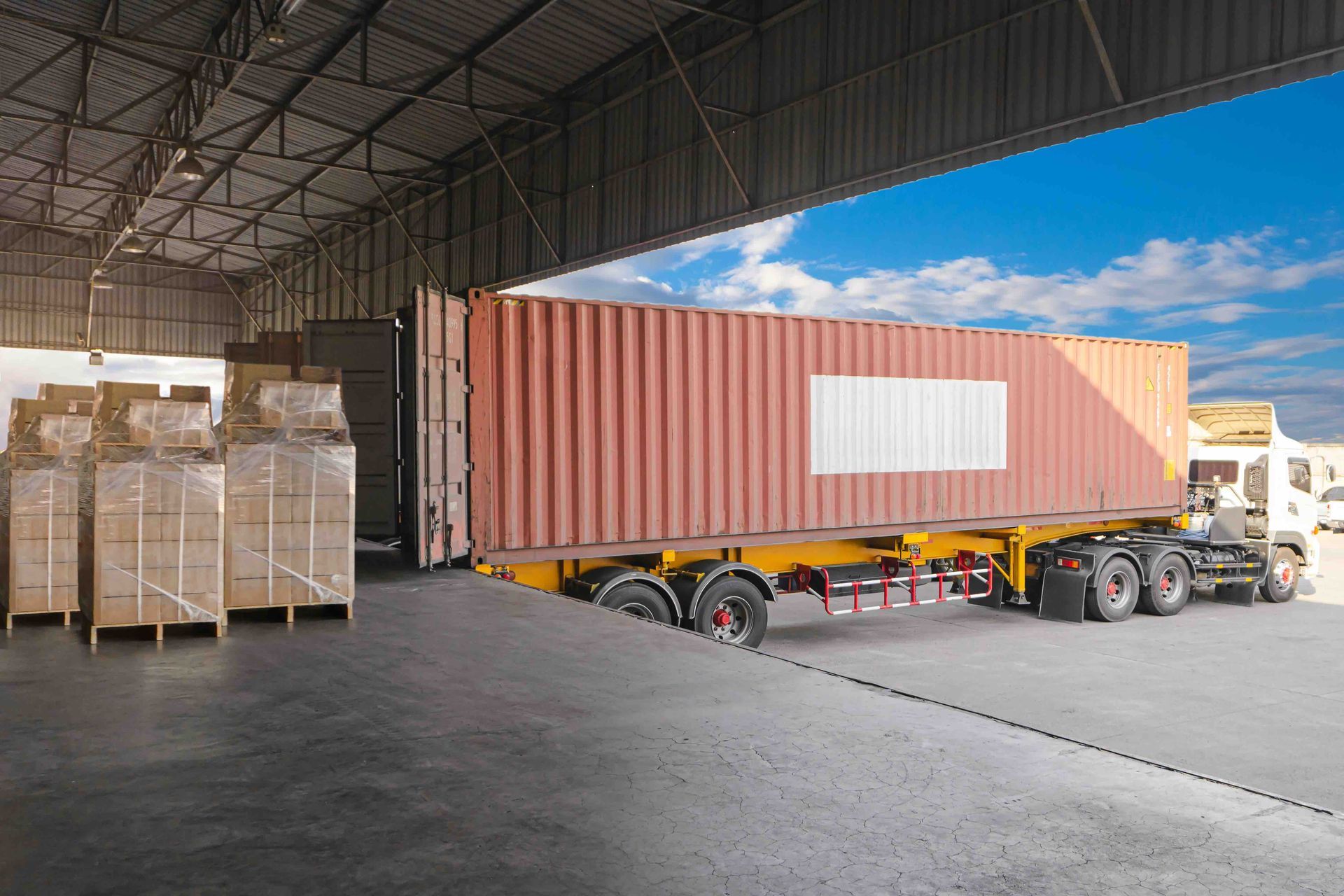 A truck is loading a shipping container into a warehouse.