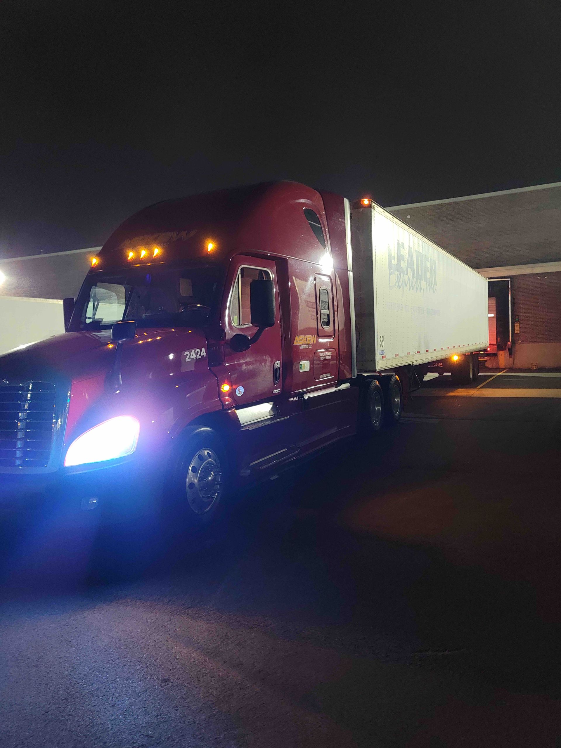A red semi truck is parked in a parking lot at night.