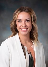 A woman is wearing a white jacket and smiling for the camera.