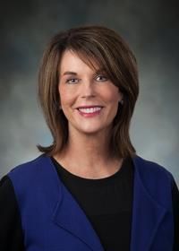 A woman wearing a blue vest and a black shirt is smiling for the camera.