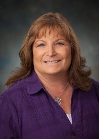 A woman in a purple shirt is smiling for the camera.