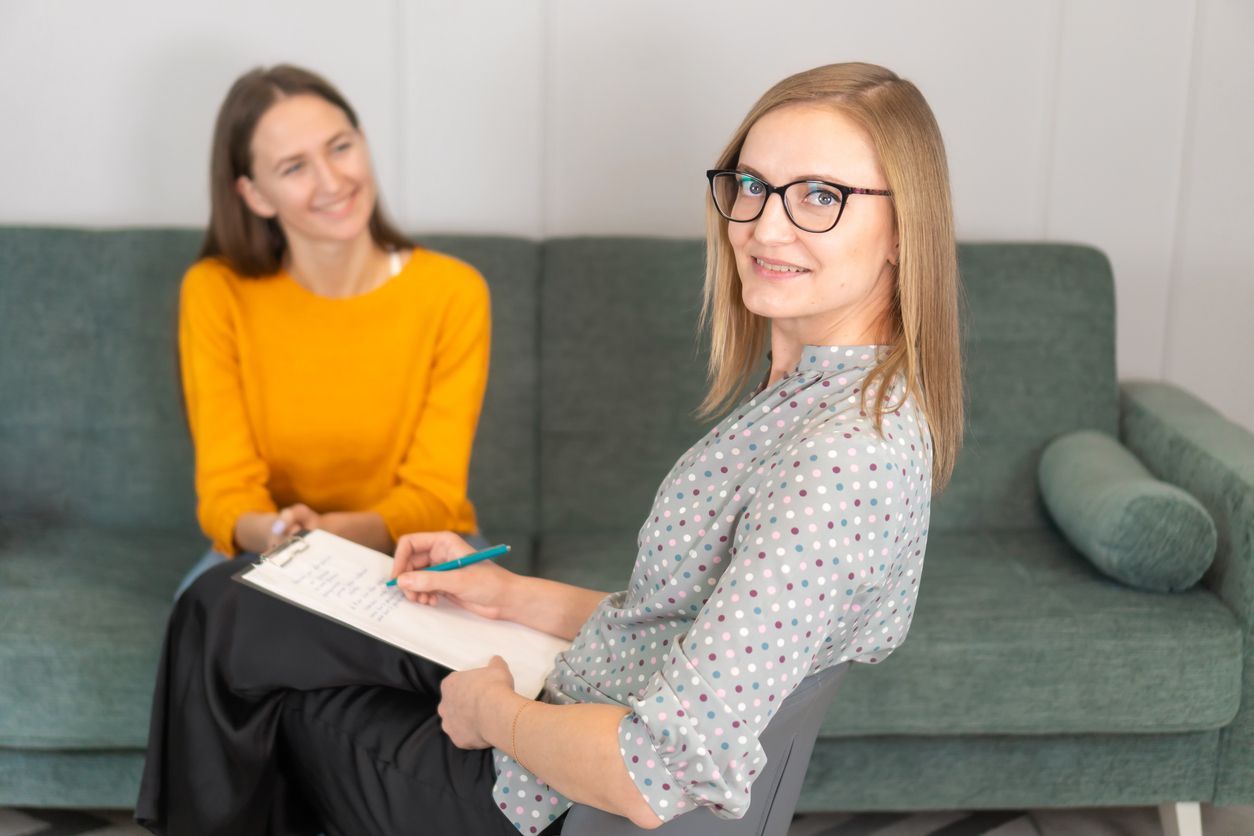 A woman is sitting on a couch talking to another woman.