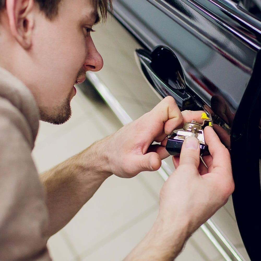 A Man Is Holding a Key in Front of A Car Door — Century Locksmiths In Toowoomba City, QLD