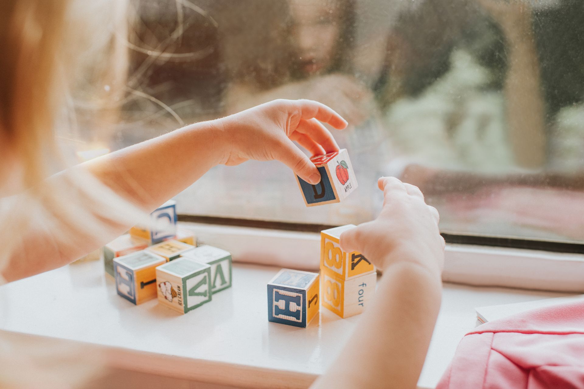 A little girl is playing with blocks on a window sill.