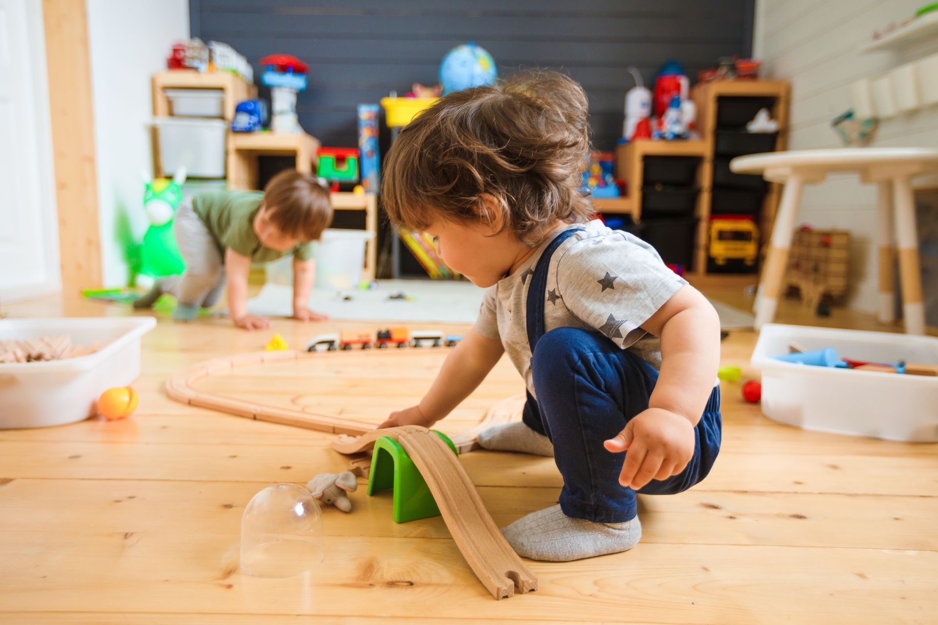 Two young boys are playing with a wooden train set on the floor.