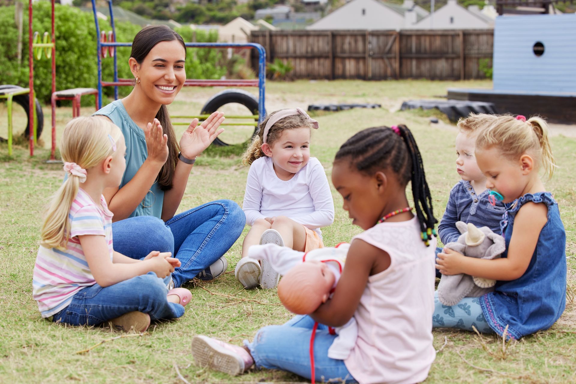 A group of children are sitting on the grass playing with a doll.