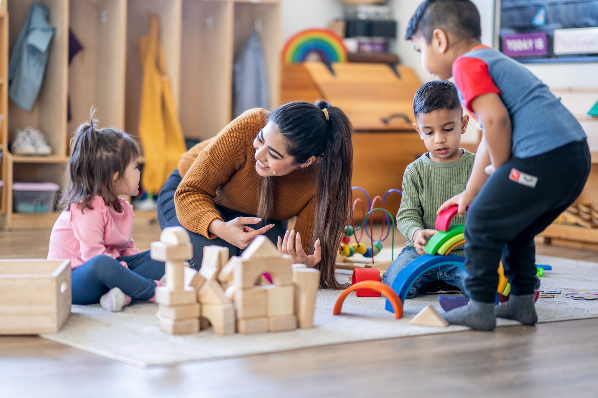 A woman is playing with blocks with children in a classroom.