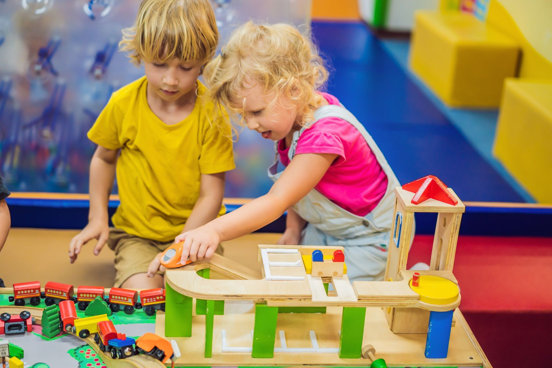 A boy and a girl are playing with a wooden toy train set.