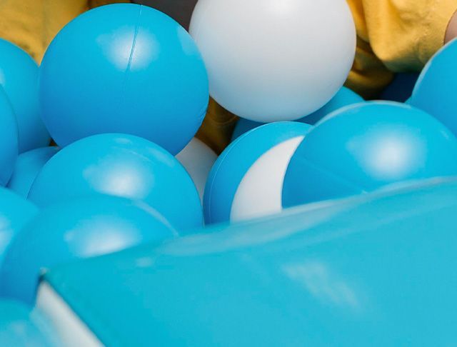 Een persoon speelt in een ballenbak gevuld met blauwe en witte ballen.