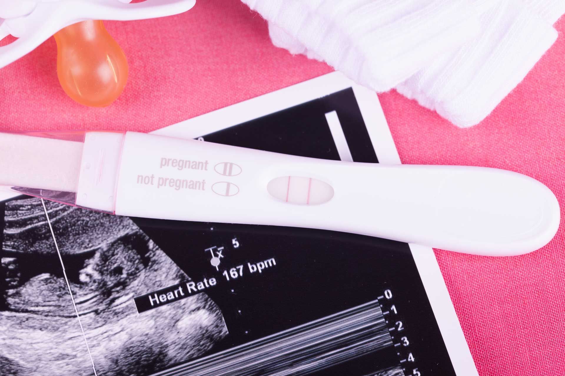 Ultrasound photo and pregnancy test with a pink background.