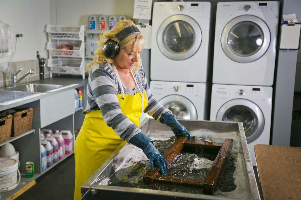 A woman in a yellow apron is washing a picture frame in a laundromat.