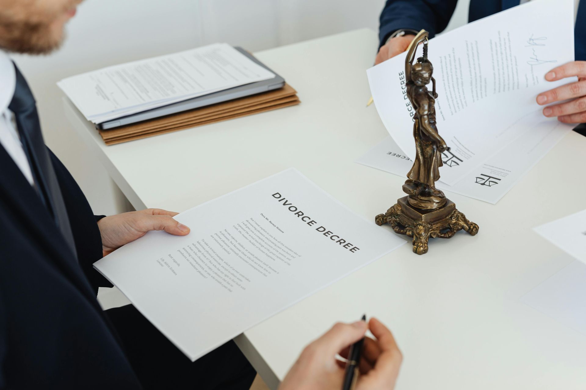 Two people are sitting at a table with papers and a statue of justice.