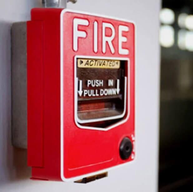 Caja roja de alarma contra incendios montada en una pared blanca, con instrucciones para empujar hacia adentro y tirar hacia abajo.