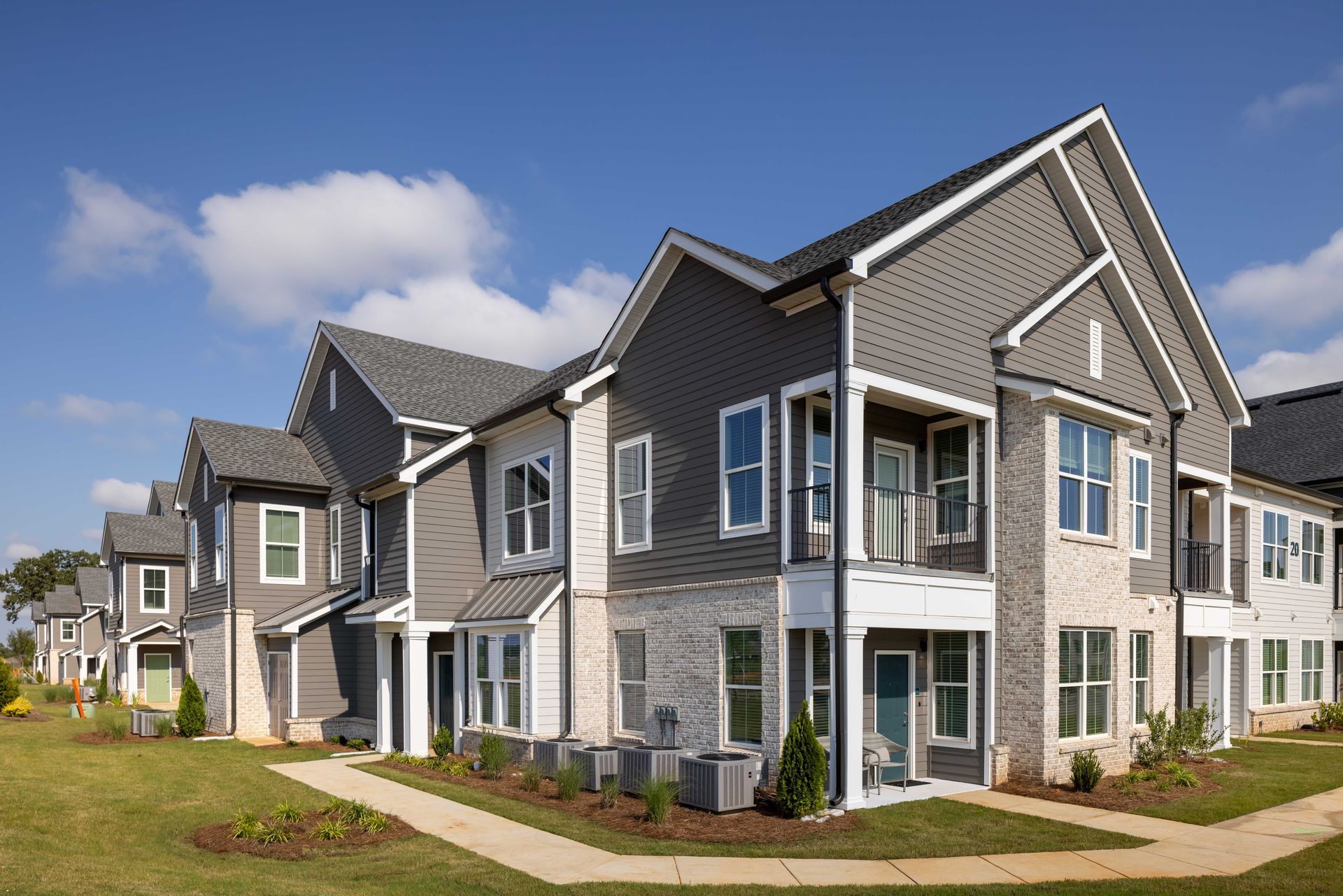 Multi-unit apartment building with gray siding, brick accents, and blue sky.