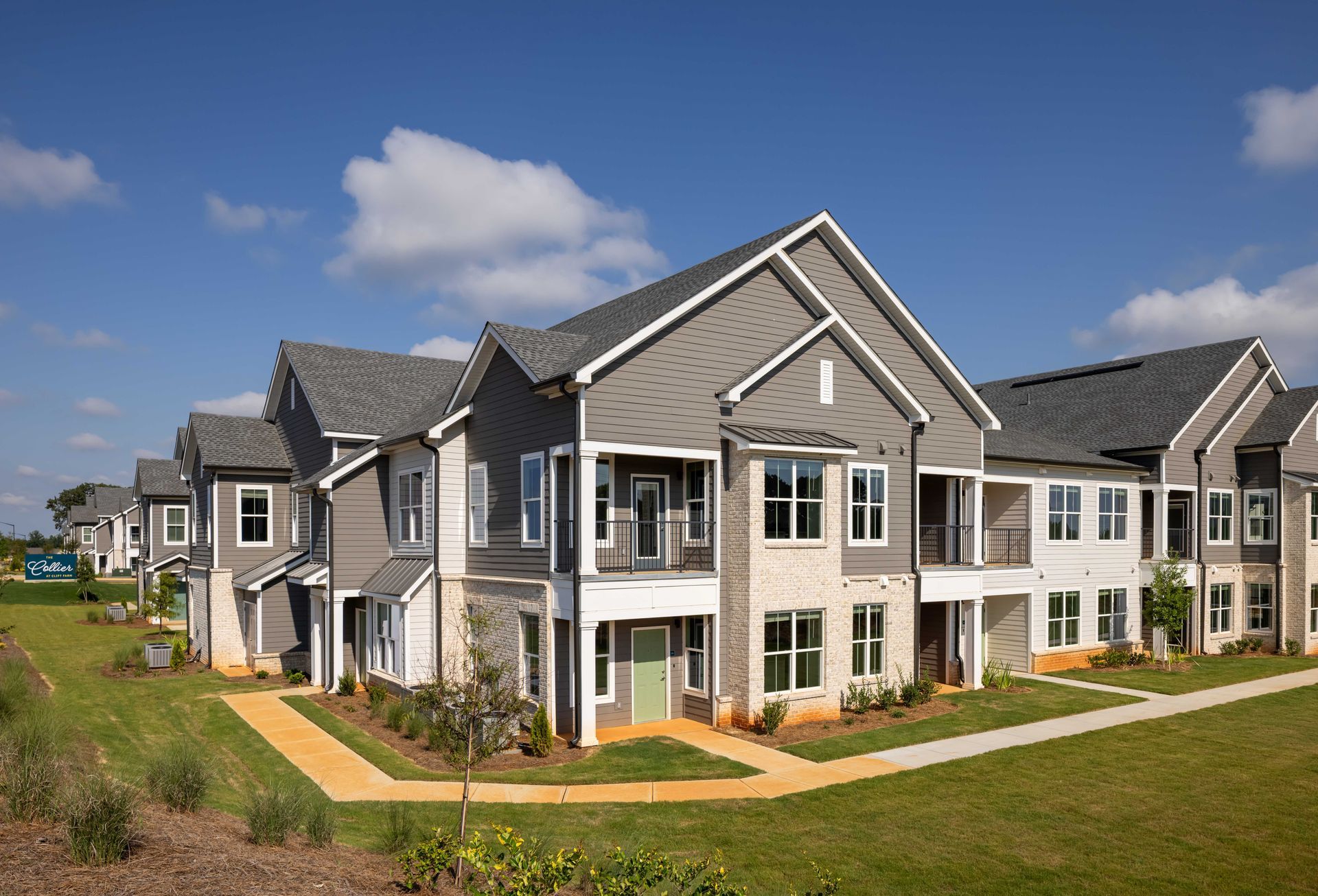 Multi-unit residential buildings, gray siding, stone accents, green door, blue sky.