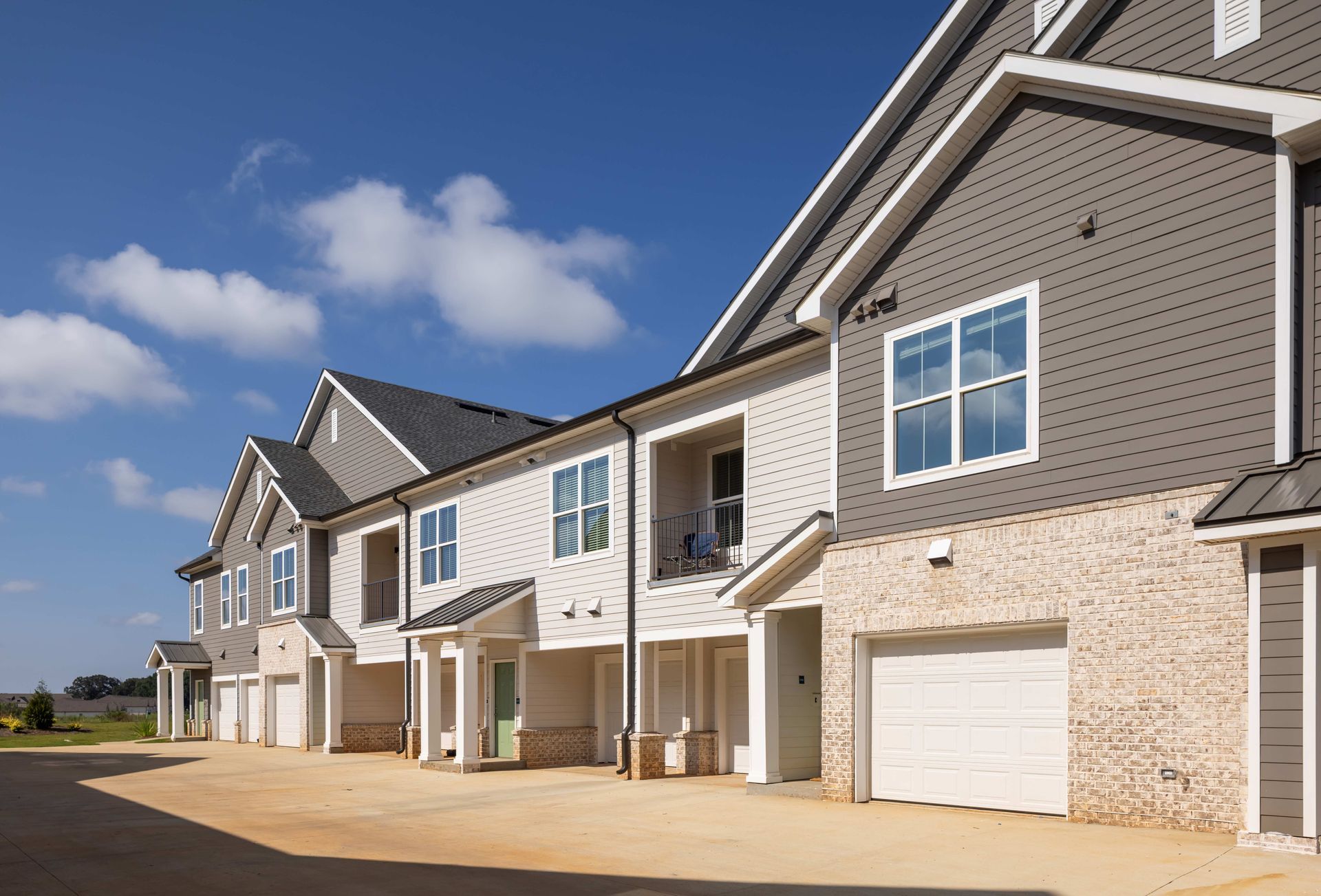 Townhomes with brick and gray siding, white trim, and attached garages under a blue sky.