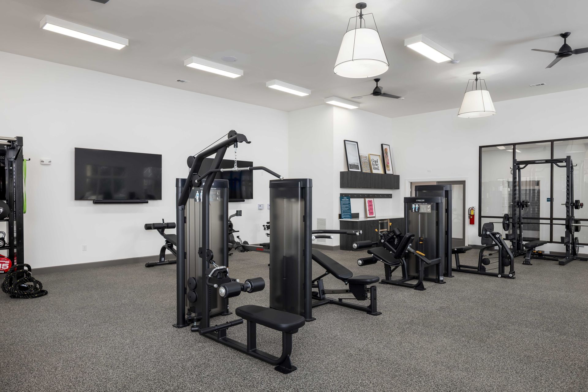 Gym with various weight machines and workout equipment on a textured floor; neutral color scheme.