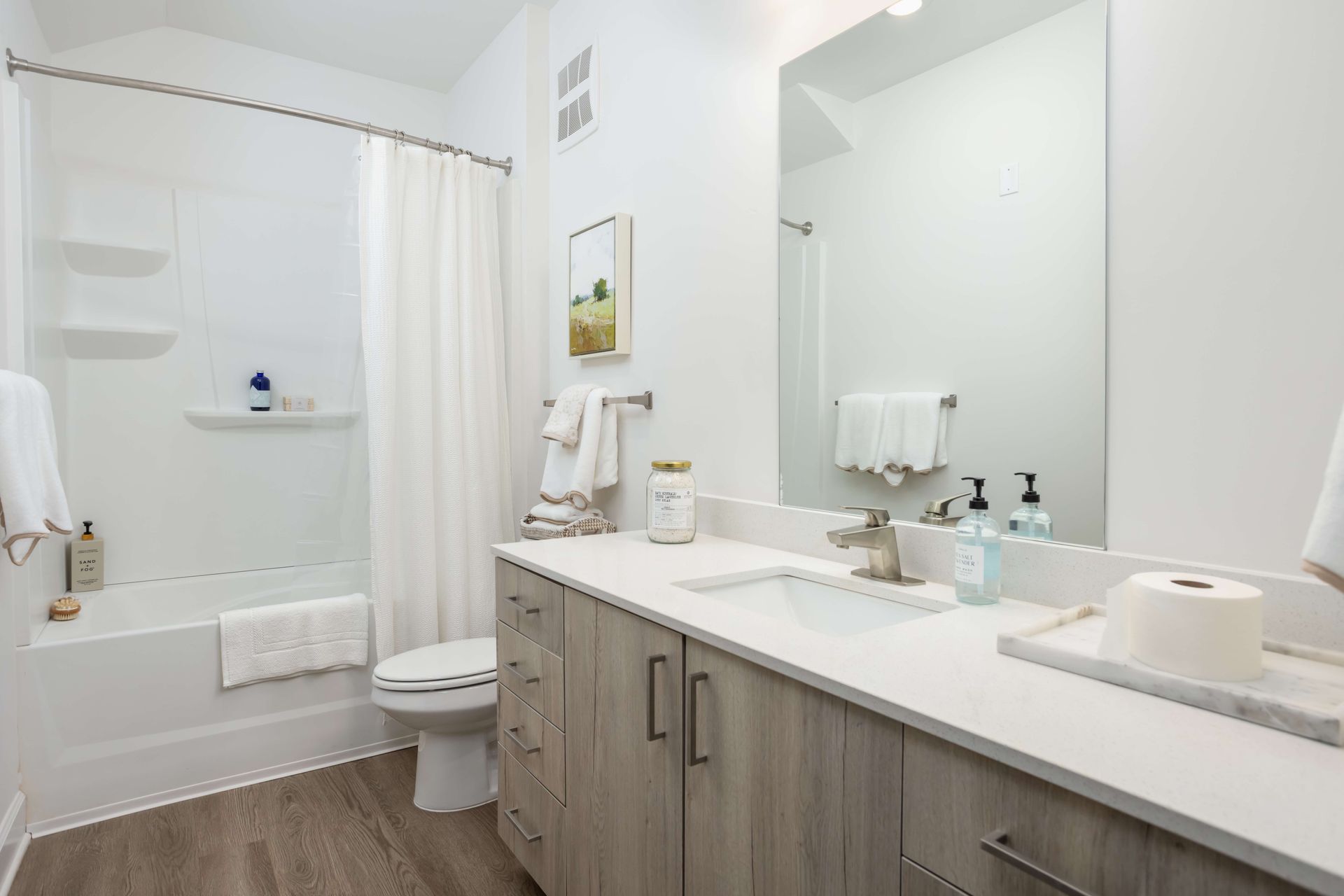 Modern bathroom with light wood cabinets, white countertop, bathtub, and large mirror.