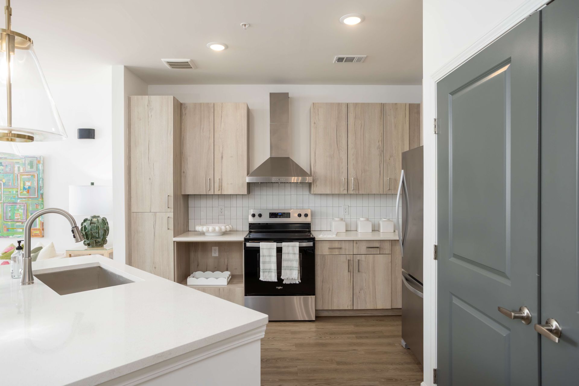 Modern kitchen with light wood cabinets, stainless steel appliances, and a white countertop.