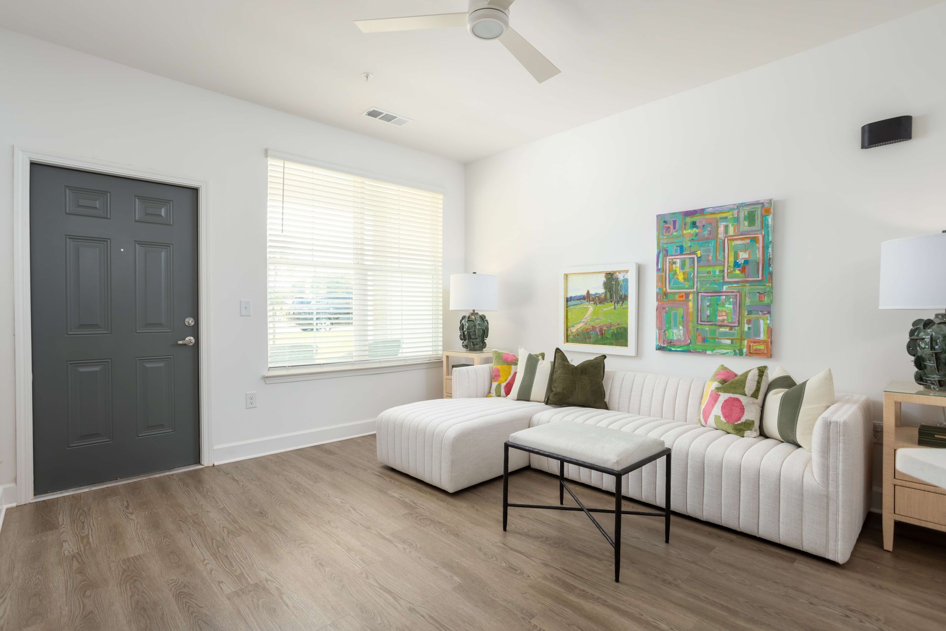 Living room with white sofa, colorful pillows, artwork, and wood-look flooring.