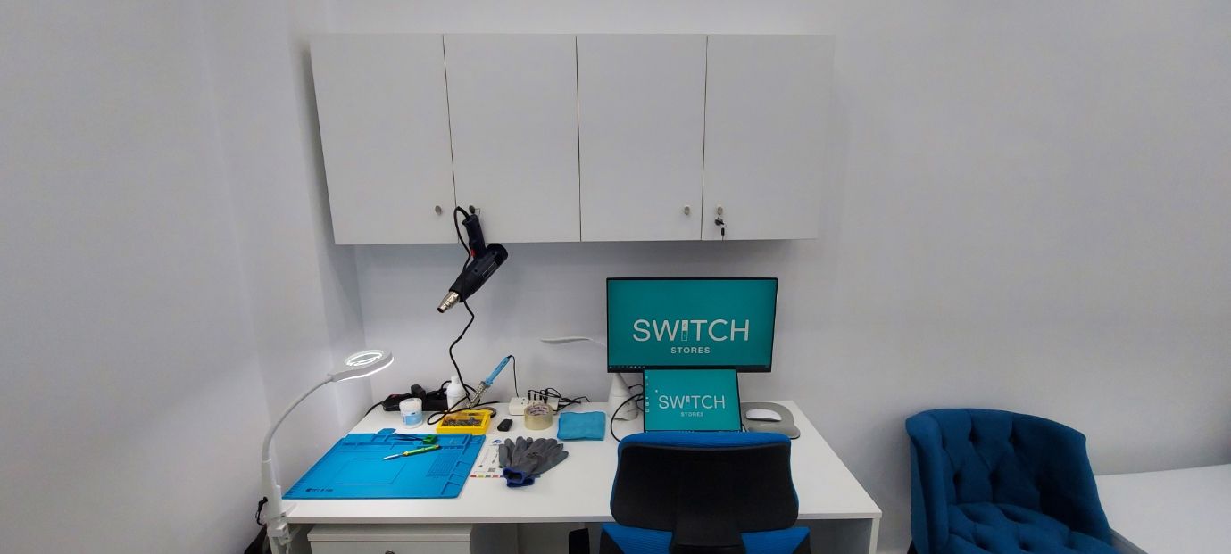 Ένα γραφείο σε ένα εργαστήριο με μια οθόνη που γράφει ΔΙΑΚΟΠΤΗΣ και μια καρέκλα. Υπάρχει εξοπλισμός για την επισκευή μικρών εξαρτημάτων.