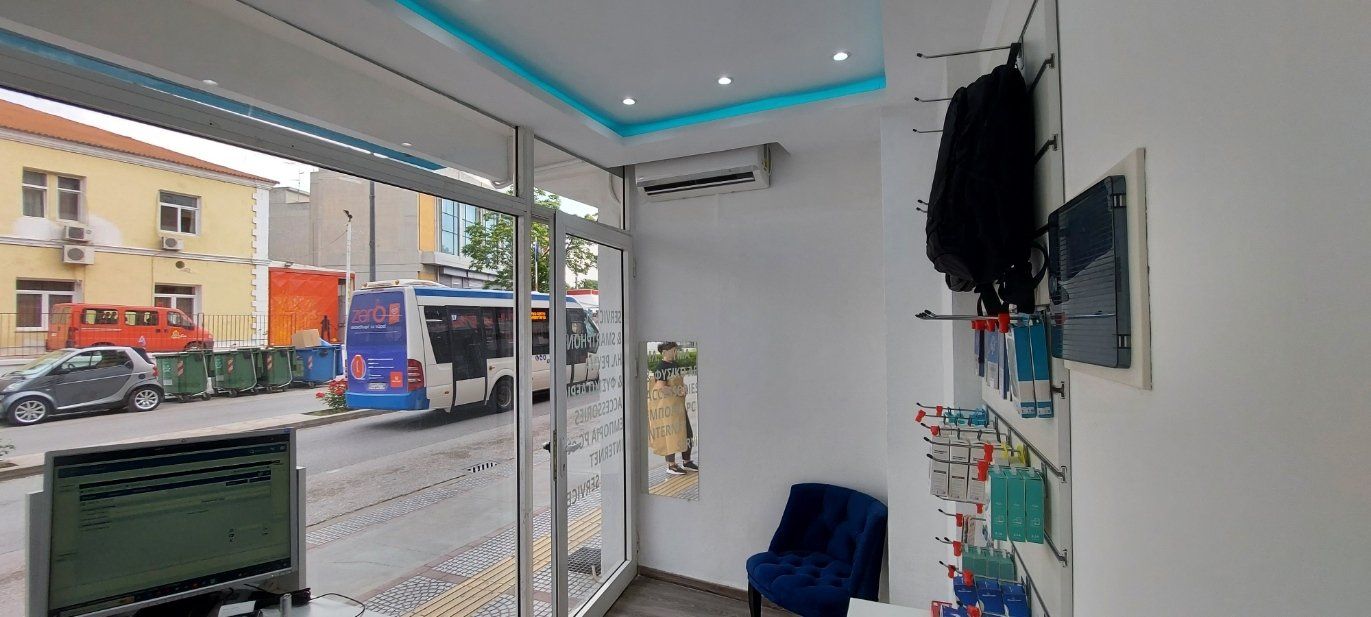 Εσωτερική φωτογραφία ενός συνεργείου επισκευής κινητών τηλεφώνων με θέα στον δρόμο. Ένα λεωφορείο και ένα κτίριο είναι ορατά μέσα από το παράθυρο.