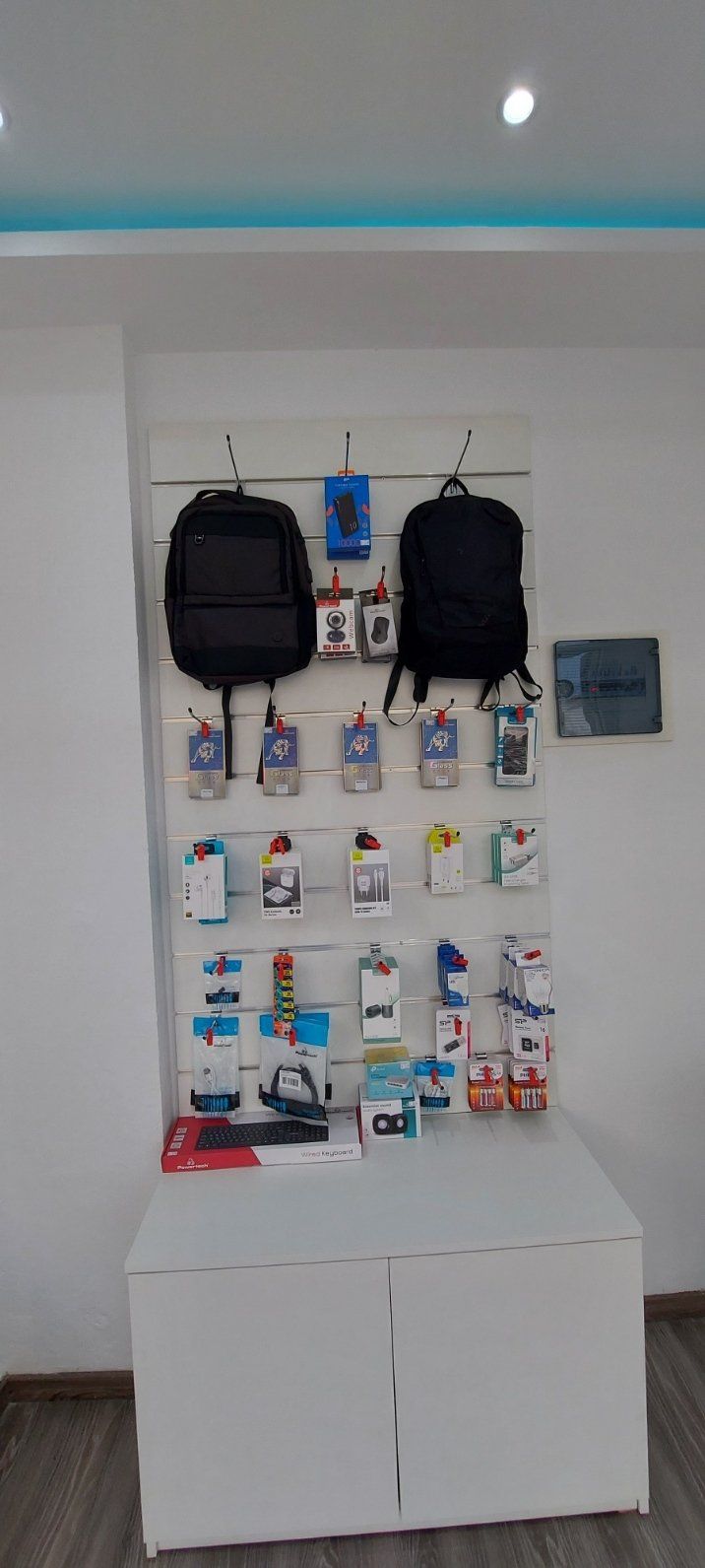 Έκθεση σακιδίων πλάτης και αξεσουάρ τεχνολογίας σε κατάστημα με λευκό πάγκο.