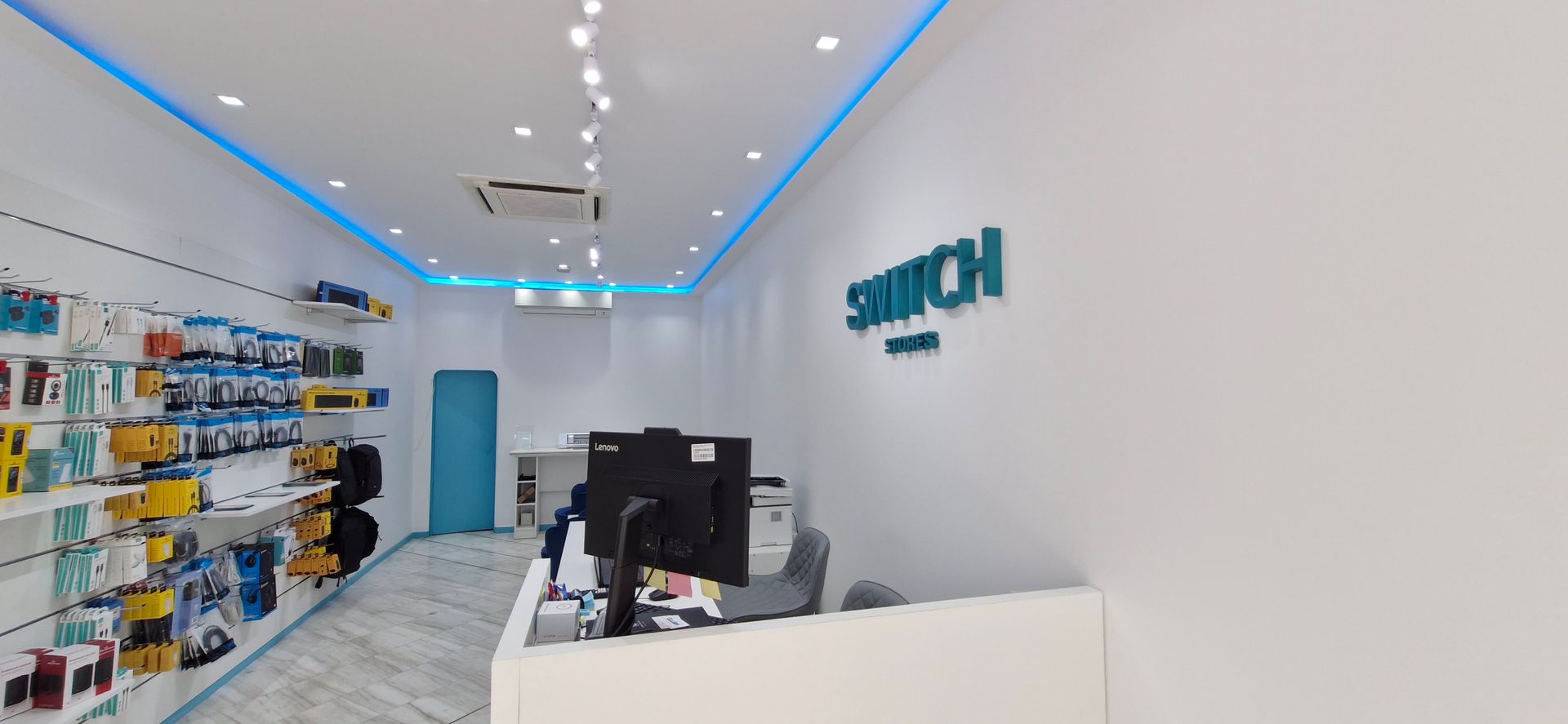 Εσωτερικό ενός καταστήματος Switch, με λευκούς τοίχους και μπλε λεπτομέρειες. Προϊόντα σε ράφια, γραφείο υποδοχής και το λογότυπο του καταστήματος.