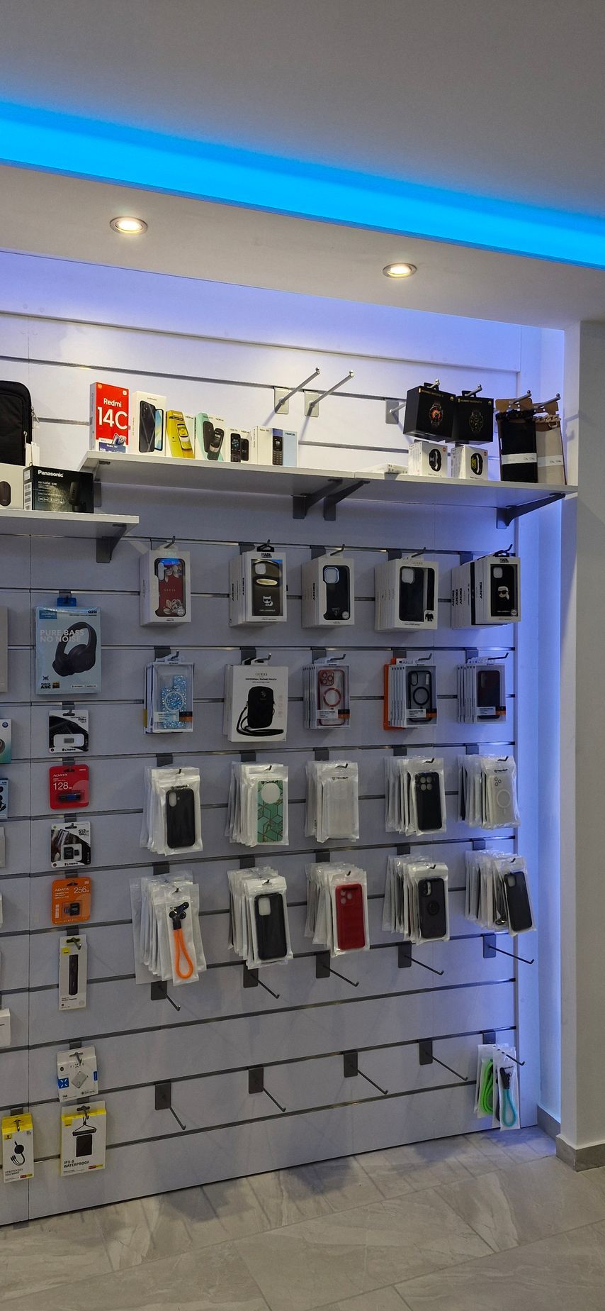 Μια λιανική έκθεση με συσκευασμένα αξεσουάρ τηλεφώνου, φωτεινά φωτισμένη κάτω από ένα μπλε φθορίζον φωτιστικό.