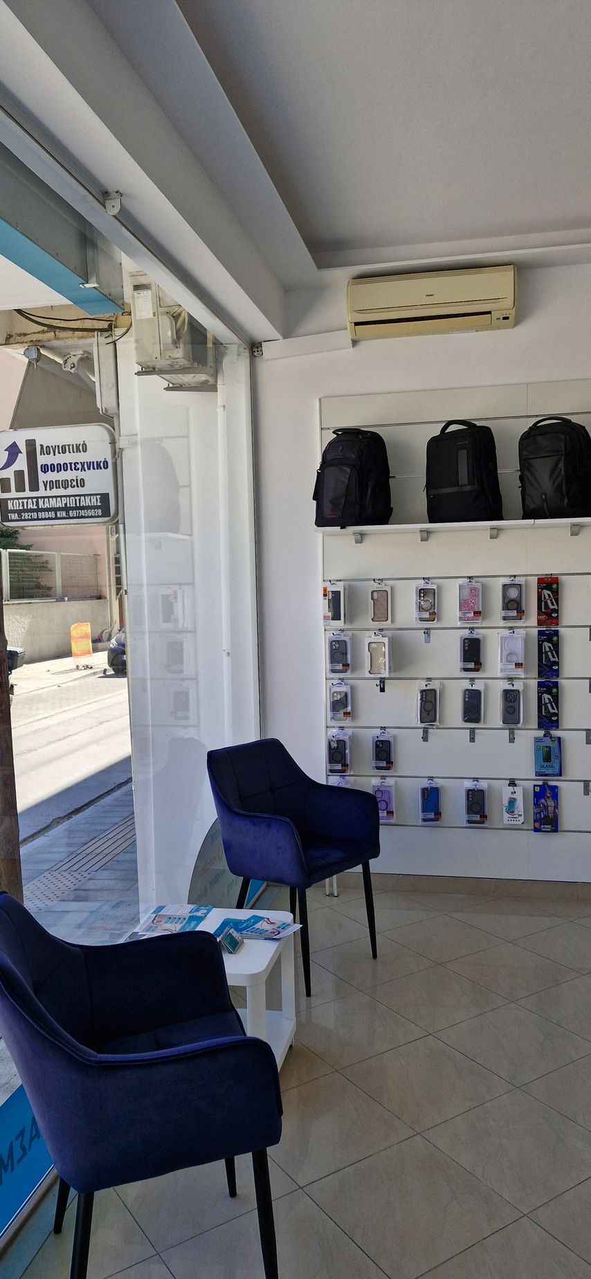 Μια εσωτερική φωτογραφία ενός καταστήματος κινητών τηλεφώνων με είδη έκθεσης, καθίσματα και σακίδια πλάτης.