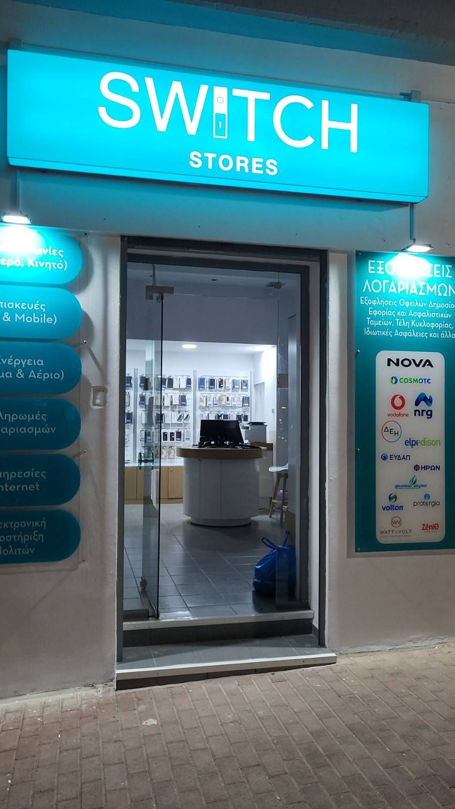 Μια βιτρίνα για τα Switch Stores, σε τιρκουάζ και λευκό χρώμα, με γυάλινη πόρτα και προϊόντα στο εσωτερικό.
