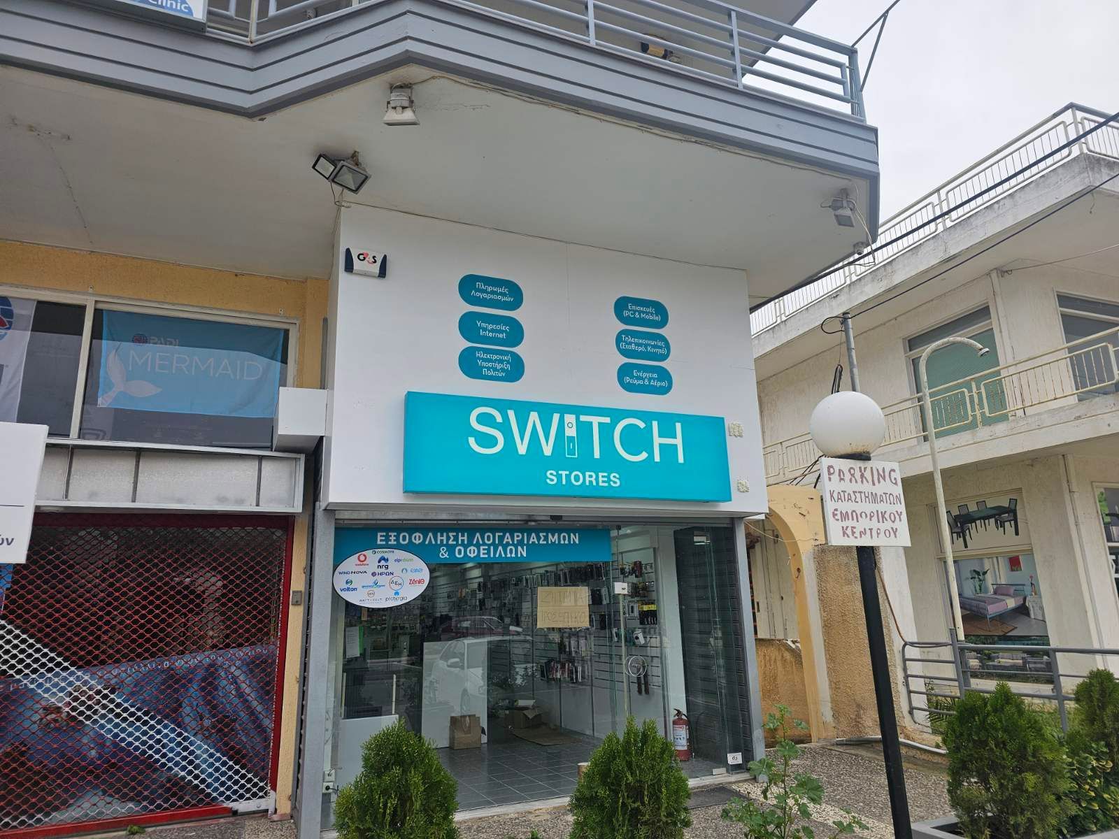 Καταστήματα Switch με γαλαζοπράσινη πινακίδα· κατάστημα με γυάλινη πρόσοψη· λευκό κτίριο.