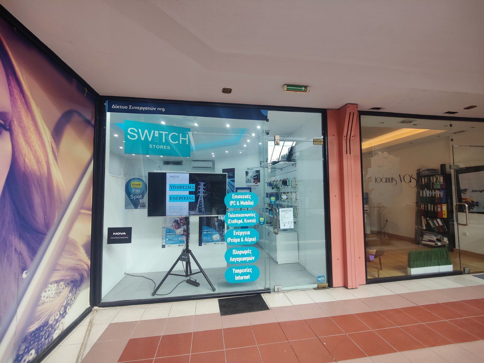 Κατάστημα Switch phone στην είσοδο ενός εμπορικού κέντρου, με οθόνες, οθόνες και μπλε λεπτομέρειες ορατά μέσα από το τζάμι.