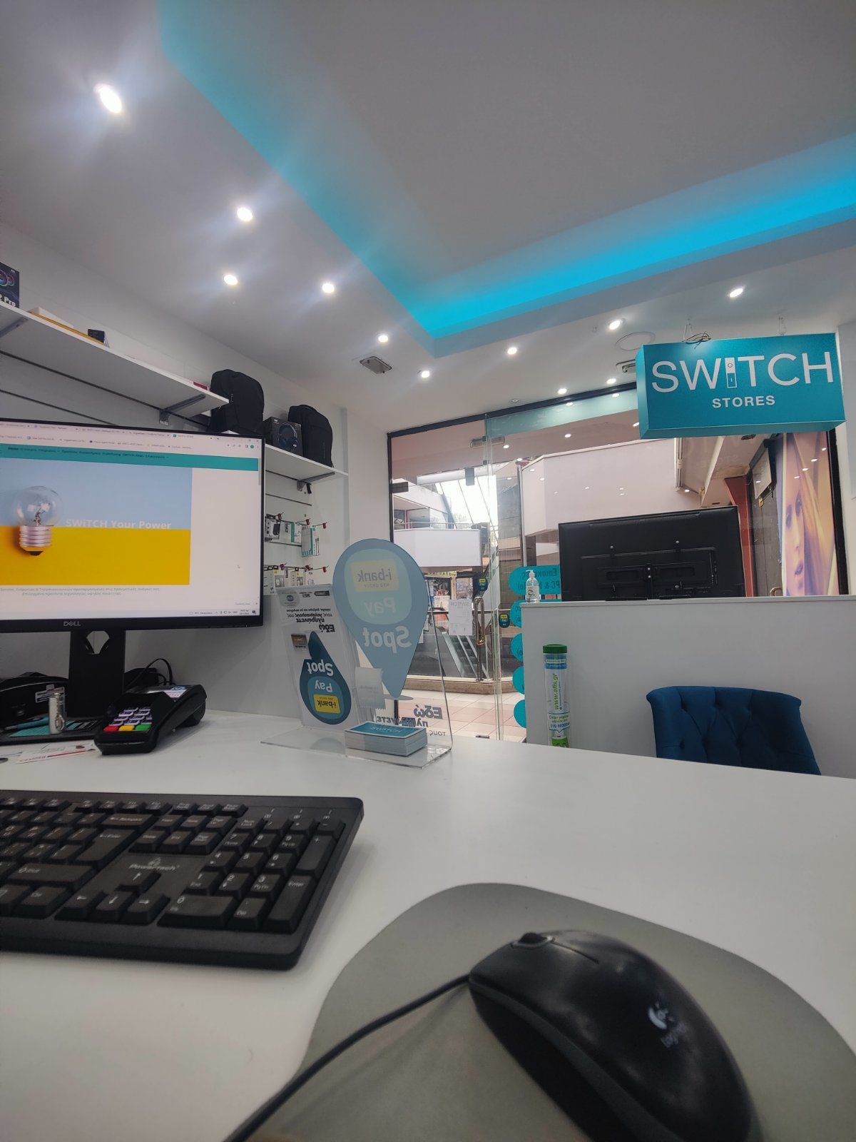 Εσωτερικό ενός καταστήματος SWITCH, με πάγκο, υπολογιστή και ανοιχτή πόρτα.