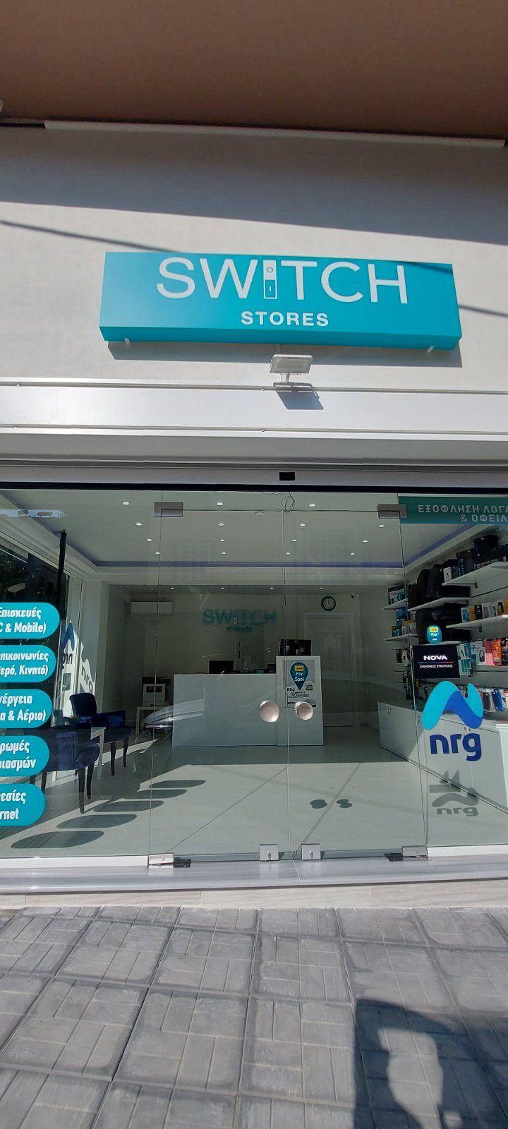 Εξωτερικό ενός καταστήματος που ονομάζεται Switch Stores με μια τιρκουάζ πινακίδα, γυάλινες πόρτες και παράθυρα.