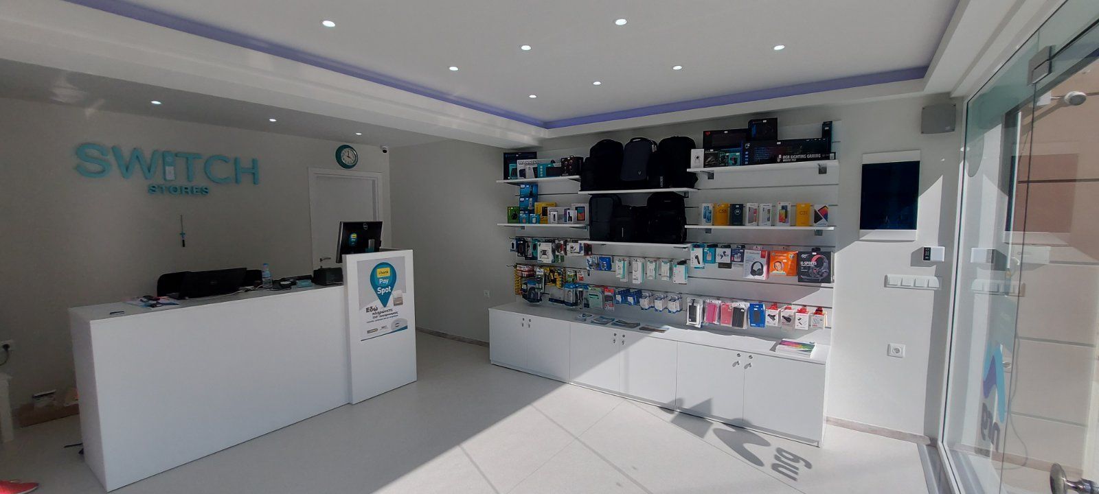 Εσωτερικό ενός καταστήματος κινητών τηλεφώνων Switch, λευκοί τοίχοι, διάφορα ηλεκτρονικά είδη σε ράφια, με ρεσεψιόν.