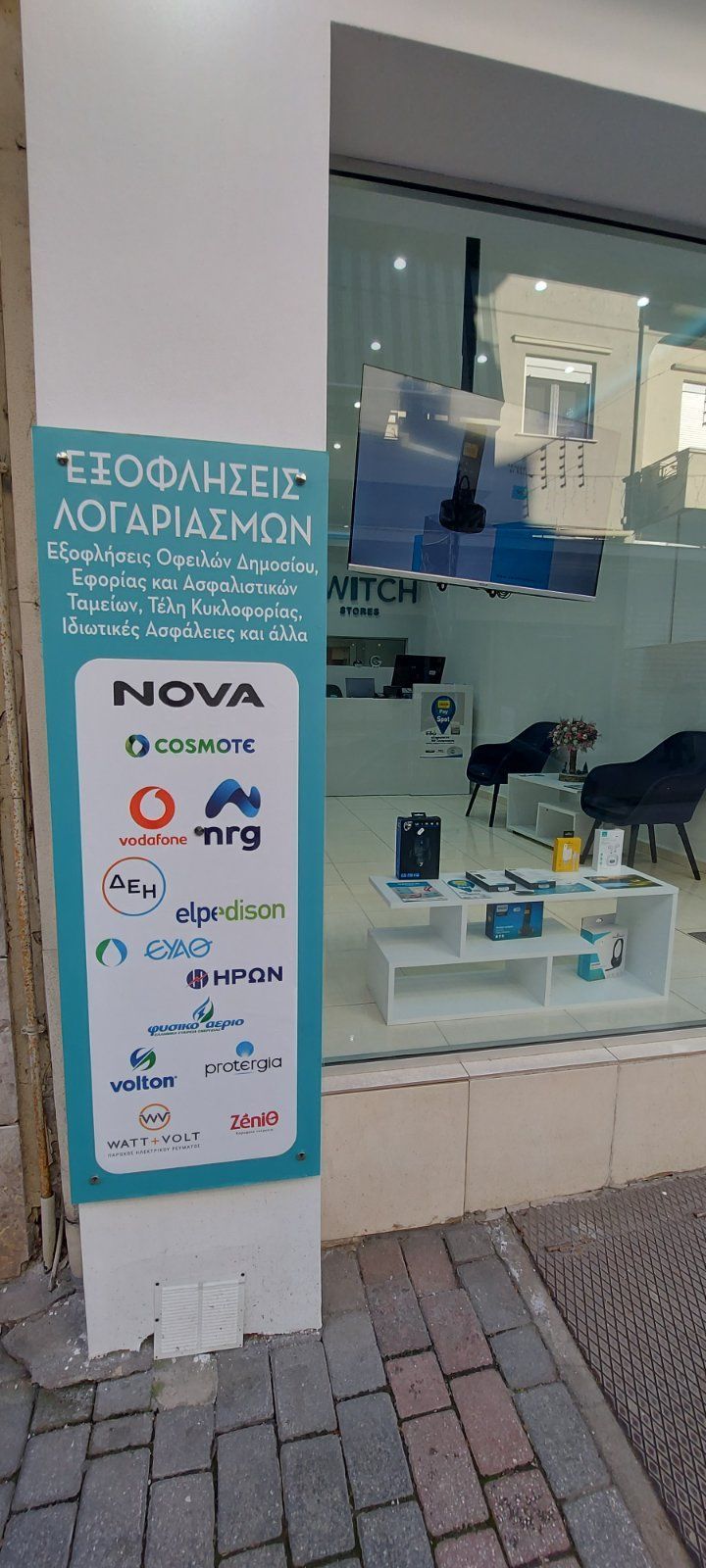 Πινακίδα που προωθεί υπηρεσίες πληρωμής λογαριασμών έξω από ένα κατάστημα με μια γαλαζοπράσινη και άσπρη πινακίδα.