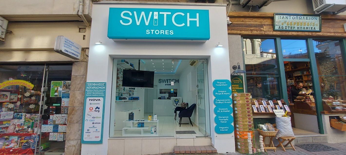 Η βιτρίνα του Switch Stores, ενός φωτεινού καταστήματος ηλεκτρονικών ειδών με μια γαλαζοπράσινη πινακίδα και βιτρίνα, πλαισιωμένη από άλλα καταστήματα.