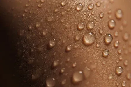 Macro shot of clear water droplets beading on textured, tan-toned skin.
