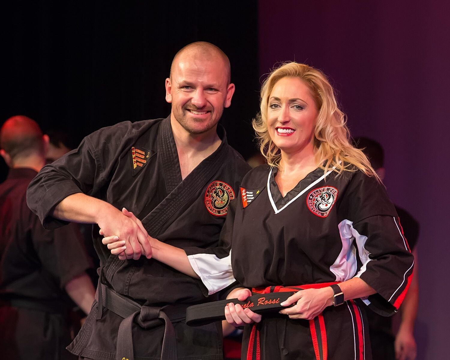 A man and a woman in martial arts uniforms are shaking hands