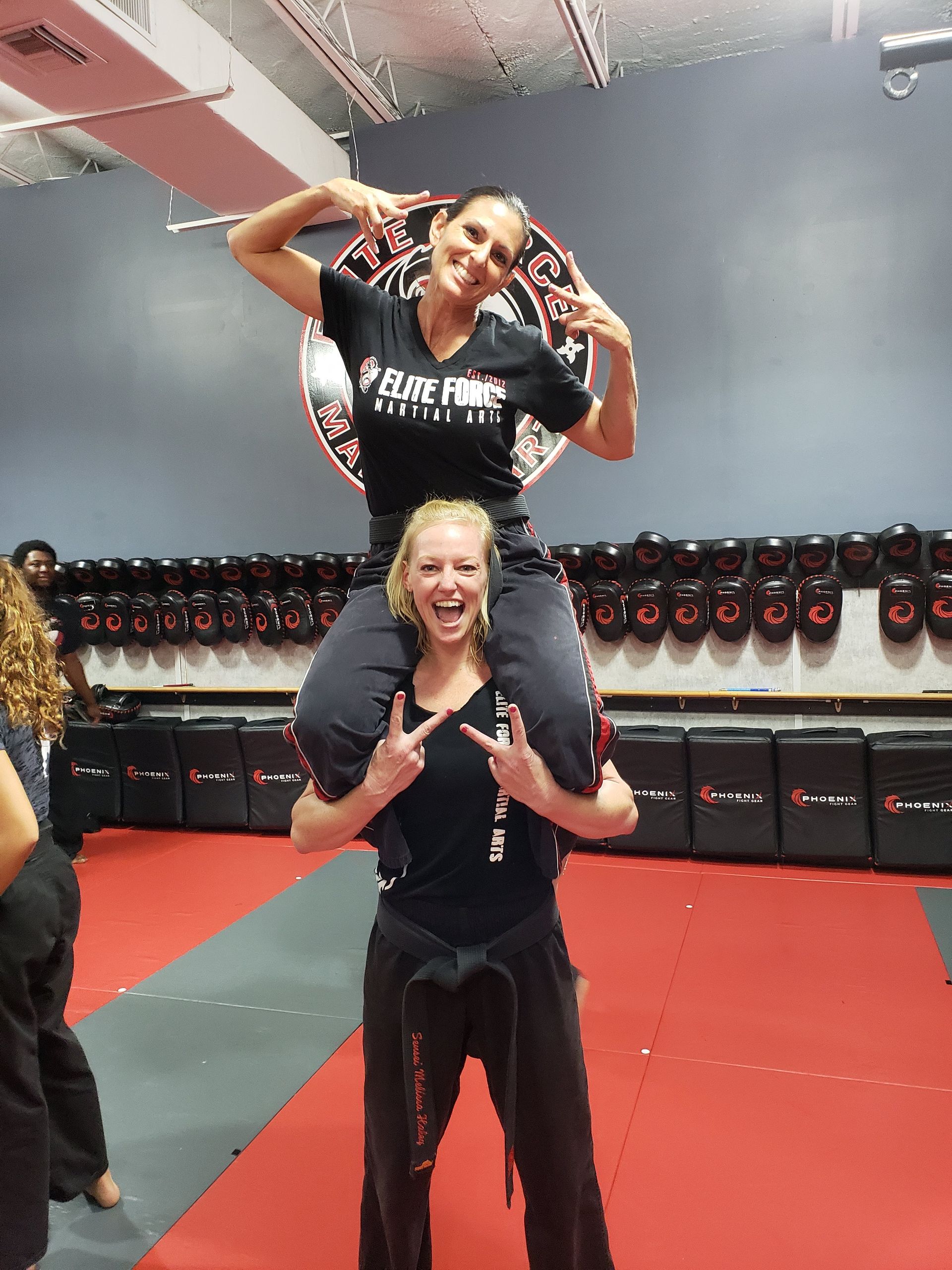 A man is carrying a woman on his shoulders in a gym.