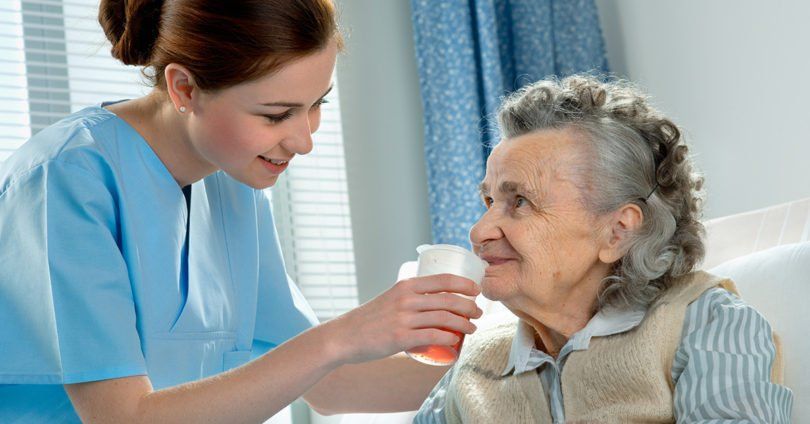Nurse feeding an elderly female patient.