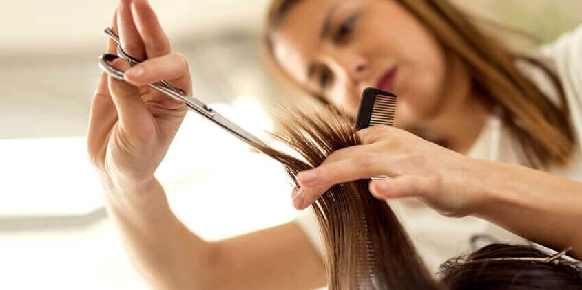 Caucasian female hair stylist cuts brown hair.
