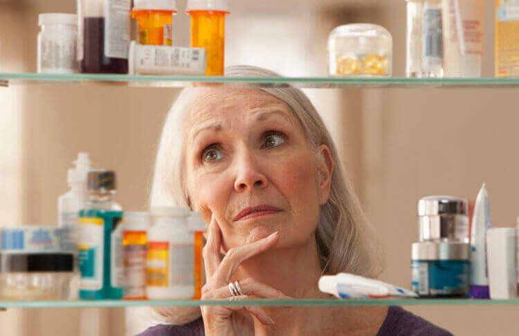 older woman thinking at her medicine cabinet