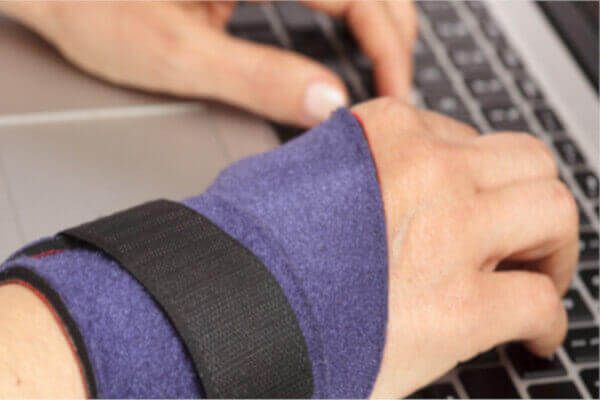 Wearig a blue wrist brace while typing on a keyboard.