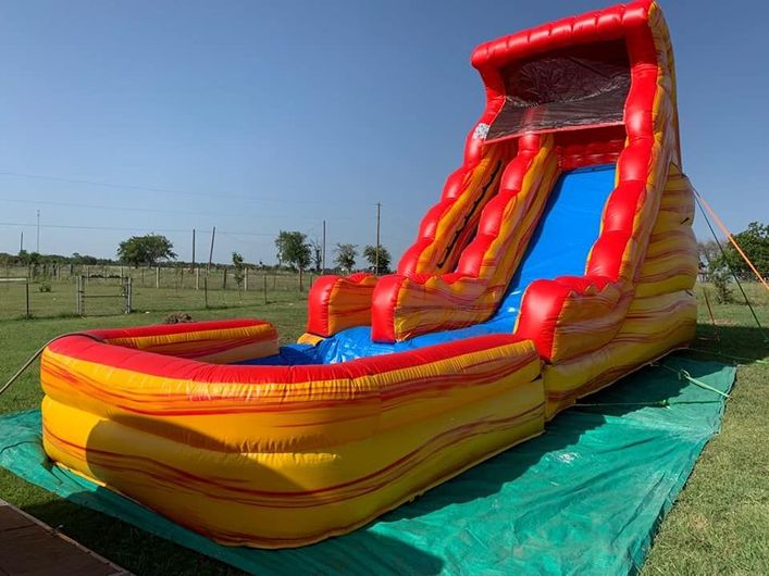 An inflatable water slide, colored red, yellow, and blue, set up on a grassy field under a clear blue sky.