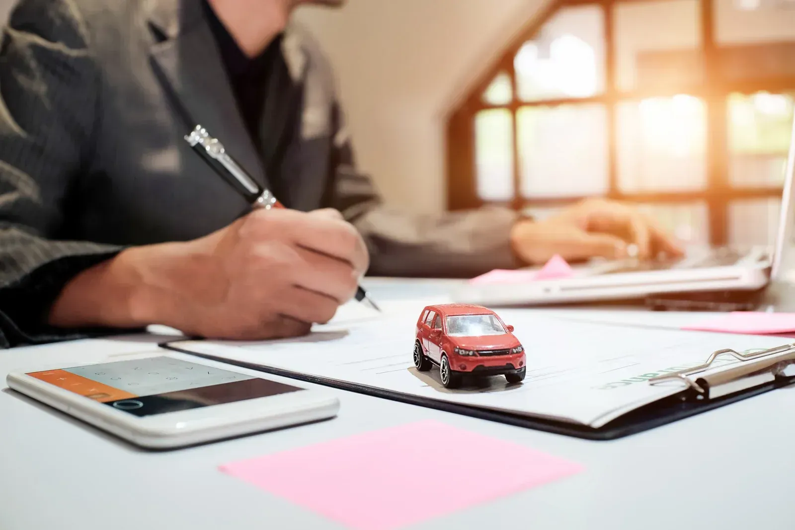 A man is sitting at a desk writing on a piece of paper next to a toy car.